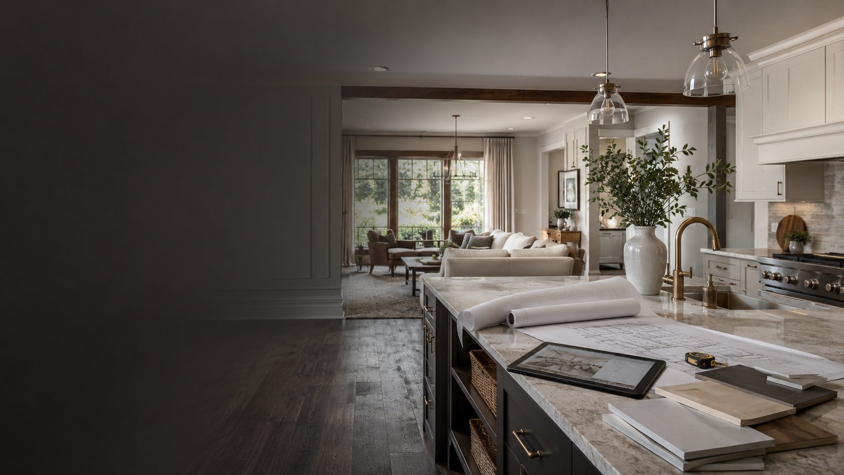 Modern kitchen with dark island counter, hanging glass pendant light, and view into neutral-toned living room with seating area